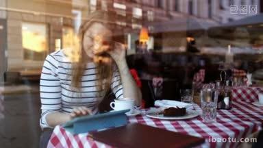 年轻女子在咖啡馆用触摸板吃甜点，透过玻璃看城市和人的倒影