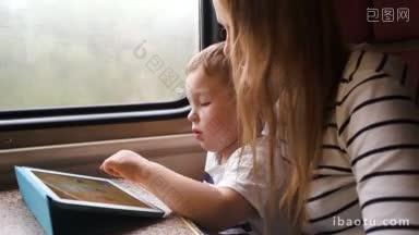 母亲看着她的小儿子在触摸板上玩，他们坐在<strong>行驶</strong>的<strong>火车</strong>的窗口
