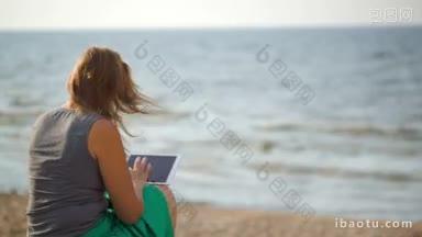 <strong>背面</strong>的女人坐在沙滩上，在一个有风的夏天，使用平板<strong>电脑</strong>
