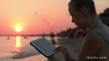 快乐的年轻女子在海滩上<strong>使用</strong>平板电脑在日落傍晚的太阳
