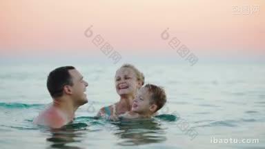 年轻幸福的父母带着儿子在海里洗澡，男孩和爸爸玩耍，亲吻他