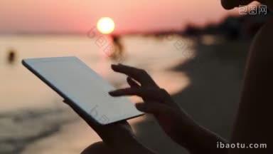 近距离拍摄的女孩使用触控板坐在海岸在日落分散人们的注意力