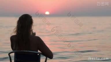 背影的女人坐在椅子上与<strong>鸡尾酒</strong>和享受美丽的日落在海上