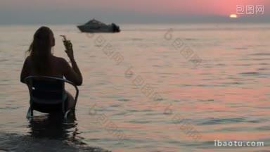 背影的女人喝鸡尾酒在海滩上，她坐在椅子上的水，<strong>享受</strong>海景