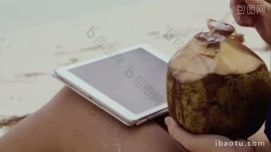 一个女人在<strong>沙滩</strong>上用平板电脑打字，喝椰子的特写镜头