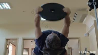低角度拍摄的一个人锻炼与重量磁盘，他移动它上下躺在长凳上