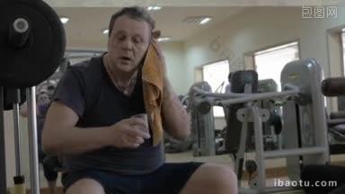 疲惫的男子在健身房锻炼后休息，用毛巾擦了擦头，喝了点水