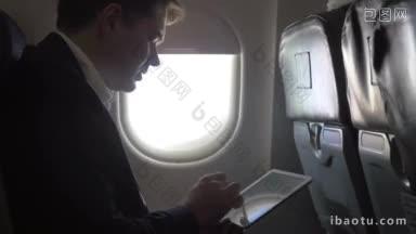 年轻的商人乘飞机旅行和工作时，他坐在照明灯旁边，在平板电脑上打字
