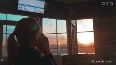 在机场候机楼里，女人一边打电话，一边望着窗外夕阳的景色
