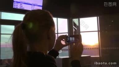 年轻女子在机场用智能手机拍窗外的日落