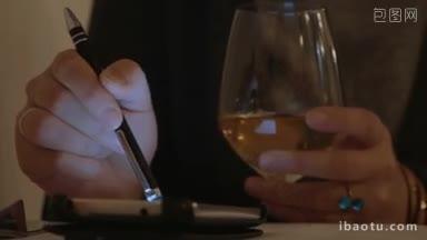 一个女人在咖啡馆喝白葡萄酒，用钢笔使用智能手机的特写镜头