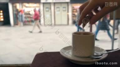 一名女子把糖倒进咖啡里搅拌，在咖啡馆里享受热饮，窗外是街道