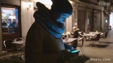斯坦尼康拍摄的一个女人使用智能<strong>手机</strong>附近的户外咖啡馆在晚上的小街上