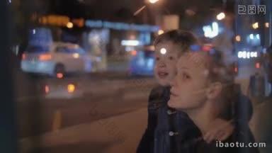 慢动作的母亲和儿子在公共汽车站的道路与繁忙的交通在晚上男孩看着