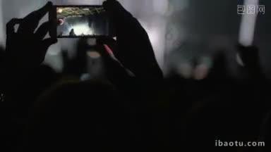 <strong>人群</strong>中手拿智能手机，在舞台上拍摄音乐表演的明亮照明
