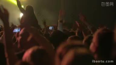 一名男子正在用智能手机拍摄音乐会的照片，他周围的人举手跳舞