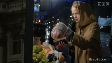 一个年轻女子在雨夜的户外水果市场上购买新鲜草莓和石榴的慢镜头