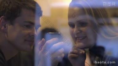 男子拿着智能<strong>手机</strong>，透过玻璃向女子展示咖啡馆里的照片