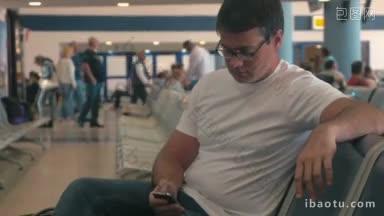 在机场或车站候机室，一个戴着眼镜拿着手机的年轻人正在上网