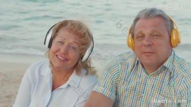 老年男女在海边戴着无线耳机听着音乐，他们享受着歌曲，和最爱的人一起跳舞