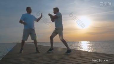 慢动作的年轻和成熟的男子有拳击锻炼在码头在日落检查反应