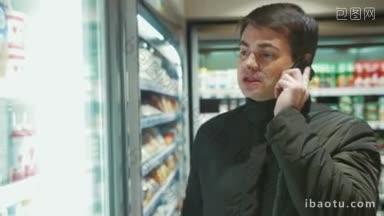 一个男人在一家食品店里一边打电话一边在冰箱里挑选饮料