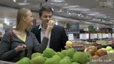 一对年轻的夫妇站在杂货店的<strong>水果摊</strong>位前，挑选苹果，并把它们放入
