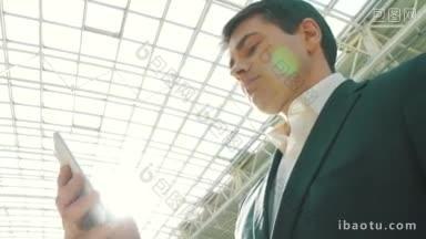 一个年轻的商人在玻璃<strong>屋顶</strong>的现代建筑中使用智能手机，阳光明亮
