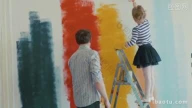 年轻的父亲和他的小女儿正在用不同的颜色粉刷墙壁，女孩正在用刷子<strong>触摸</strong>爸爸的脸