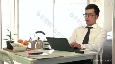 技术和亚洲人在家里用电脑工作，年轻的商人在吃早餐的时候用笔记本电脑工作