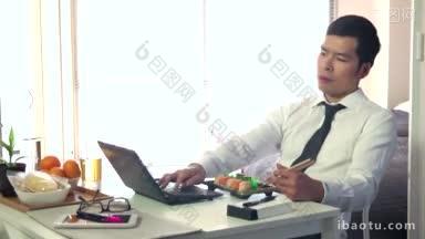 亚洲人在家里用电脑工作，年轻的商人在工作时用笔记本电脑吃饭