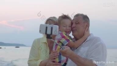 快乐的爷爷奶奶和小孙子在海边用手机自拍爷爷抱着男孩，他们用自拍杆
