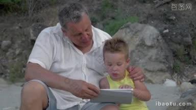 爷爷和小孙子在<strong>户外</strong>玩电脑，爷爷拥抱着他，和他说话