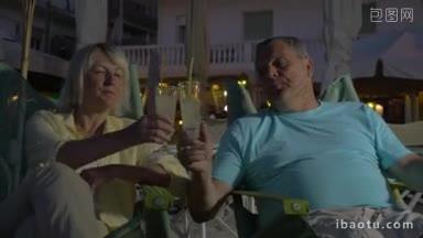 妻子和丈夫晚上坐在海滩上碰杯喝鸡尾酒
