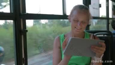 快乐的金发女<strong>人</strong>带着平板电脑坐在<strong>公交</strong>车上，她坐在窗边的平板上发短信