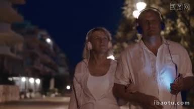 老夫妇戴着耳机在度假胜地散步，享受着音乐，在安静的夜晚一起放松