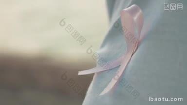 一个人穿着白色t恤上的粉色乳腺癌意识丝带的特写镜头，<strong>背景</strong>是离焦的大海