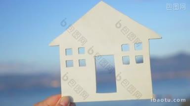 慢动作特写镜头的<strong>手</strong>握住房子模型的背景上的大海和天空的海滨房子