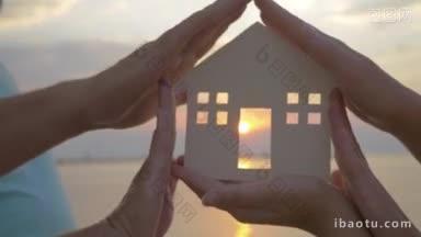 特写镜头中，手握着房子的剪影，透过房子的门可以看到落日