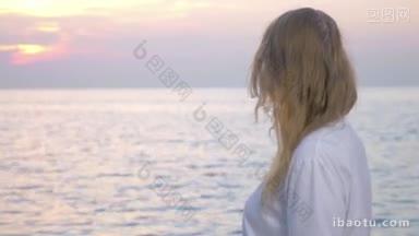 年轻的女人带着粉红色的丝带在日落的海边，她转向镜头<strong>显示</strong>乳腺癌意识的标志