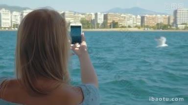 金发女人坐船旅行，用智能手机拍沿海城市和大海的慢镜头