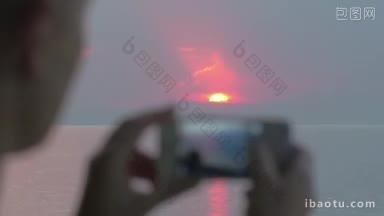 一名女子用苹果公司设计的iPhone智能<strong>手机</strong>拍摄海上日落美景的特写镜头