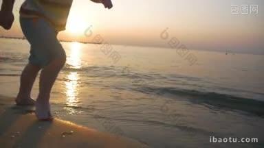 慢动作斯坦尼康拍摄的一个赤脚小男孩在温暖的阳光下沿着海边的湿沙上跑步