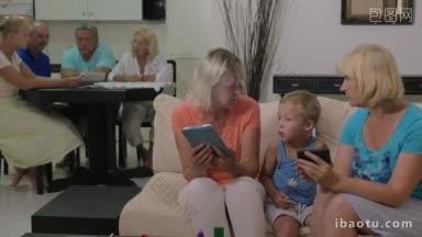 奶奶和孙子在家里，一个女人在给孩子看手<strong>机上</strong>的东西，另一个在用平板电脑