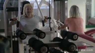 两个高级妇女在健身中心锻炼，一个人用胸压机，另一个人用拉