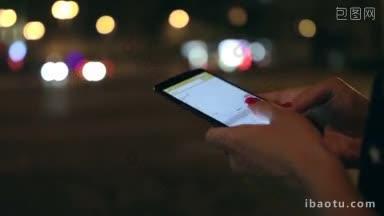 特写女人的手在深夜的街道上用手机发短信