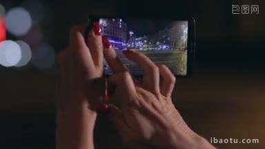 特写女子的手拿着智能手机，在街道上拍摄夜城浅景深