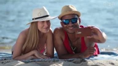 暑假快乐的情侣躺在沙滩上，以大海为背景，用手机自拍