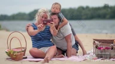 快乐的家庭和男孩在夏天的周末在河岸野餐快乐的家庭坐在彩色的毯子上