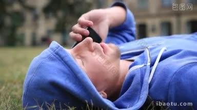 自信而成功的学生躺在学校外面的草坪上和同学用手机聊天